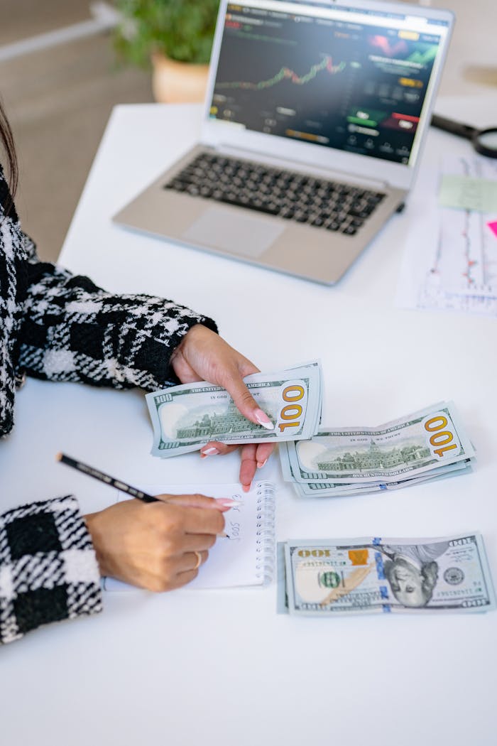 Woman counting American dollars with laptop and notes, focused on finance.